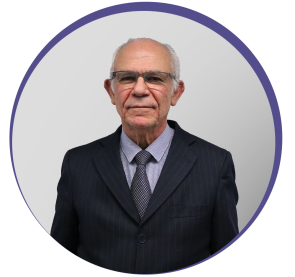 Imagem circular de homem idoso de fios brancos e óculos pousando para foto. Ele veste terno preto de listras finas na cor cinza, blusa quadriculada e gravata estampada também cinza. É o doutor Silvio Arruda Vasconcelos.