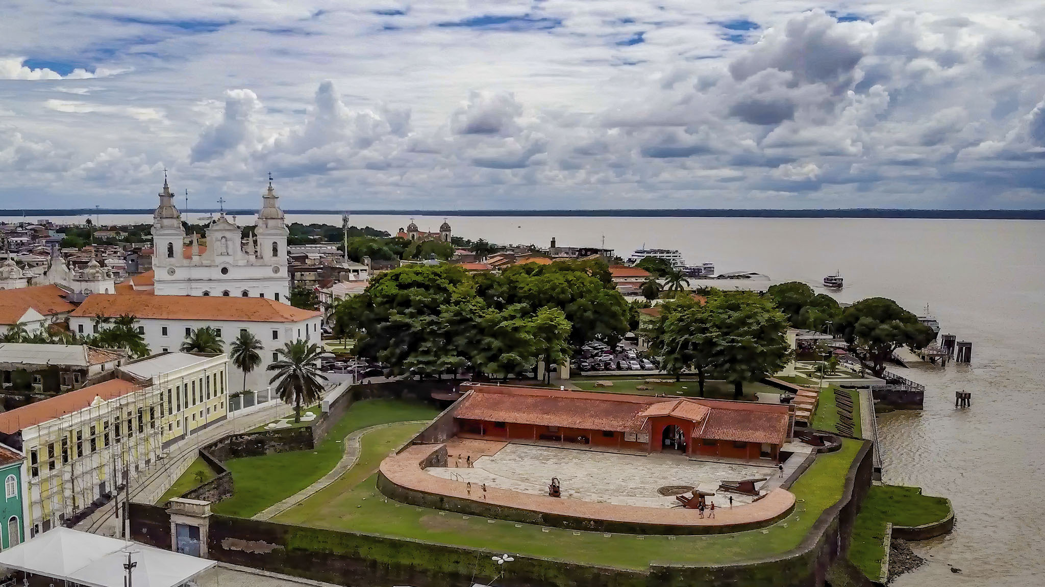 Vista geral da cidade de Belém, no Pará, sede da COP30, com igreja em destaque, o mar ao fundo e um céu azul com nuvens.