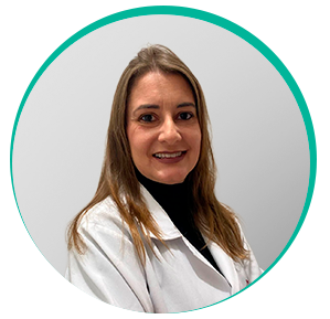 Mulher branca de cabelo liso e loiro escuro usando blusa de lã preta de gola alta e jaleco branco sorrindo para foto. É a dra. Juliany Gomes Quitzan.