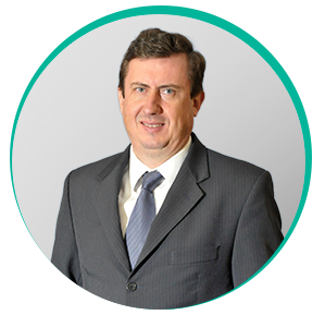 Homem branco de fios pretos e curtos e olhos azuis, vestindo terno cinza com blusa branca e gravata cinza, em pé, sorri para foto. É o dr. Paulo Marcelo Tavares.