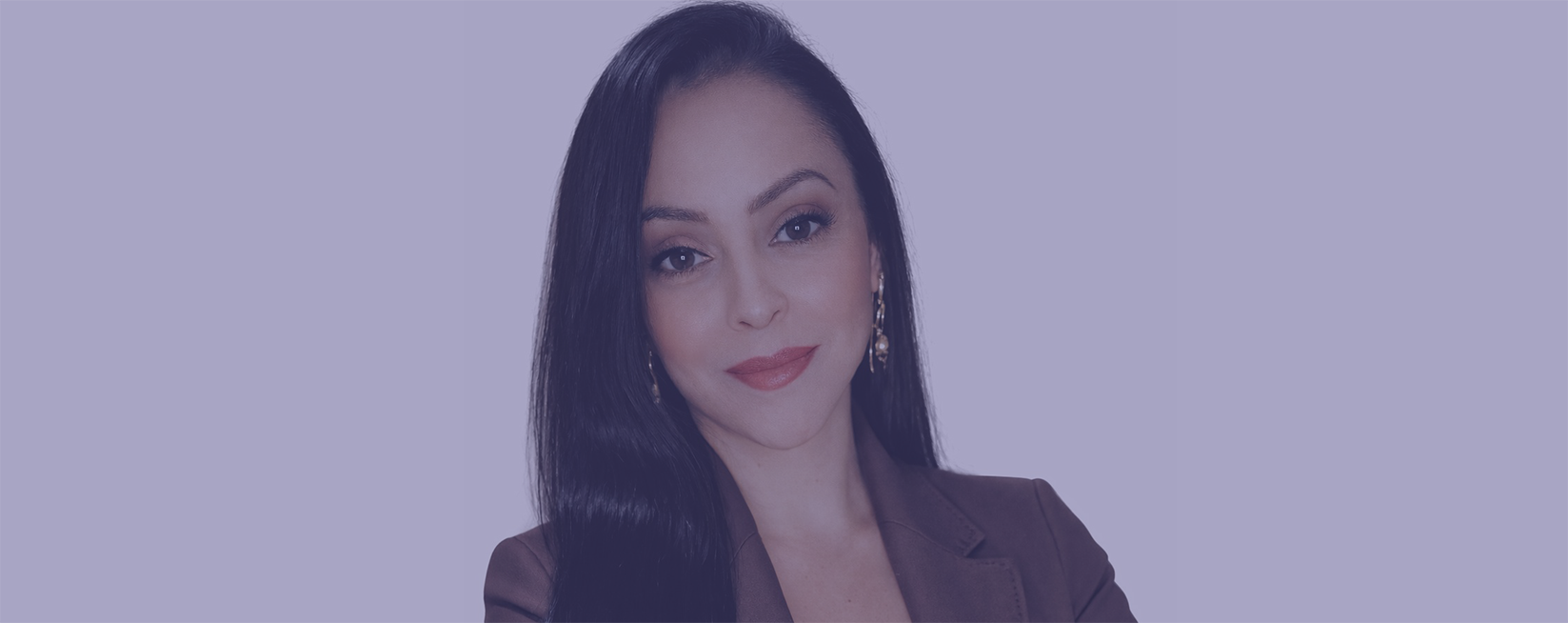 Mulher jovem, morena, de cabelos lisos, longos e pretos, e olhos amendoados. Apresenta um leve sorriso no rosto e usa um terninho marrom. Esta é Esther Espejo.