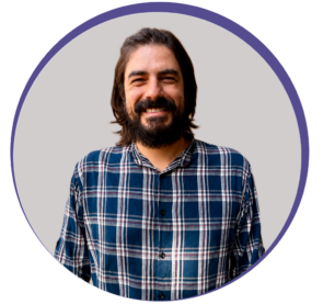 Bruno_Alonso_Miotto_1 Homem branco com cabelos longos e repicados na altura dos ombros, barba e bigode castanhos. Usa uma camisa xadrez e sorri para a foto. Esse é Bruno Miotto.